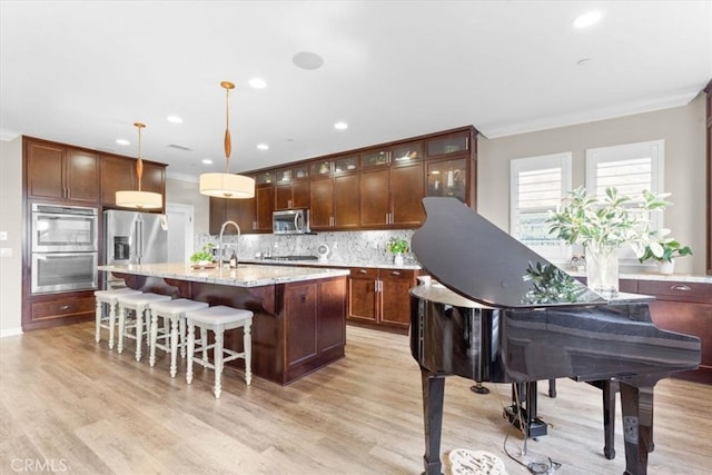 kitchen featuring glass insert cabinets, appliances with stainless steel finishes, a kitchen island with sink, crown molding, and pendant lighting