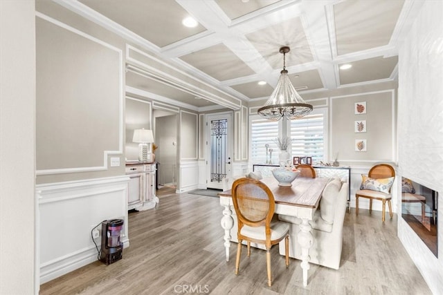 dining area featuring coffered ceiling, ornamental molding, light wood-style floors, a chandelier, and a decorative wall