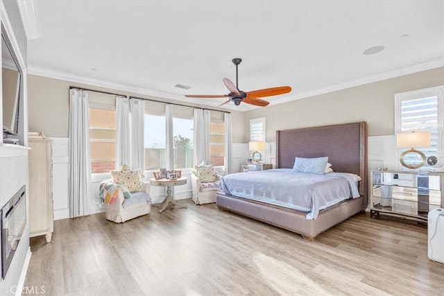 bedroom with light wood finished floors, visible vents, wainscoting, crown molding, and a fireplace