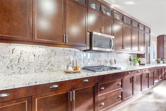 kitchen featuring decorative backsplash, glass insert cabinets, appliances with stainless steel finishes, light stone counters, and crown molding