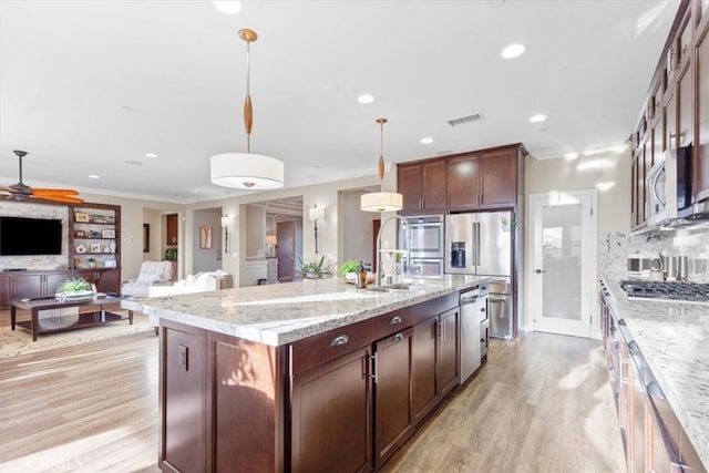 kitchen with light stone counters, stainless steel appliances, hanging light fixtures, open floor plan, and a kitchen island with sink