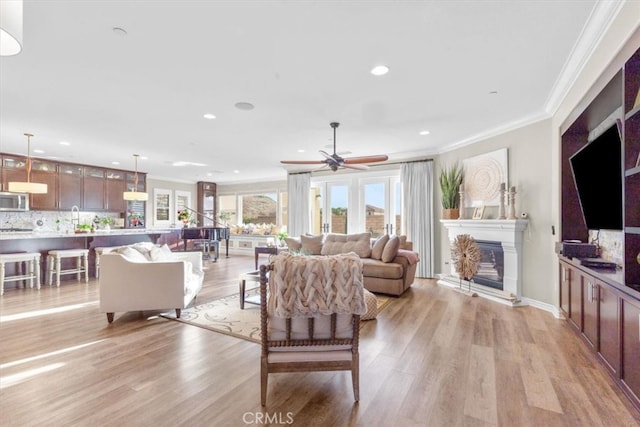 living area with a glass covered fireplace, crown molding, light wood-style flooring, and recessed lighting