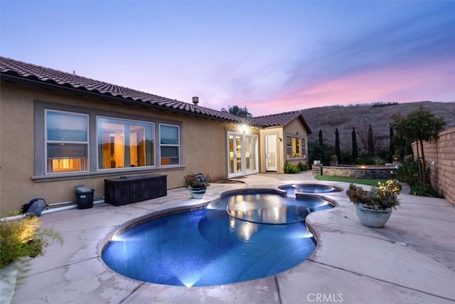 pool at dusk featuring a pool with connected hot tub, fence, french doors, and a patio