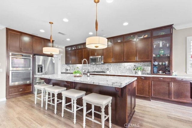 kitchen with glass insert cabinets, pendant lighting, appliances with stainless steel finishes, and light stone countertops