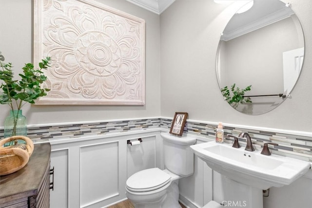 bathroom featuring a wainscoted wall, ornamental molding, a sink, and toilet