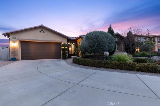 view of front of property featuring concrete driveway, an attached garage, a tiled roof, and stucco siding