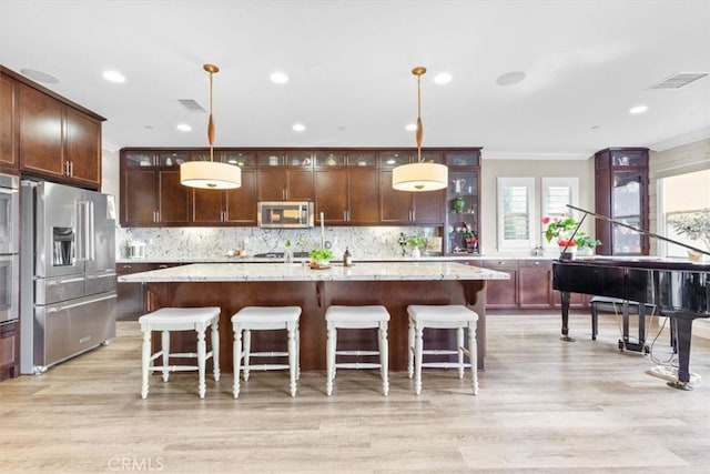 kitchen featuring tasteful backsplash, appliances with stainless steel finishes, light stone counters, a kitchen island with sink, and pendant lighting