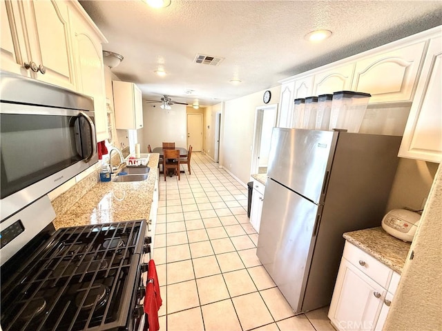 kitchen with appliances with stainless steel finishes, sink, light tile patterned floors, ceiling fan, and light stone countertops