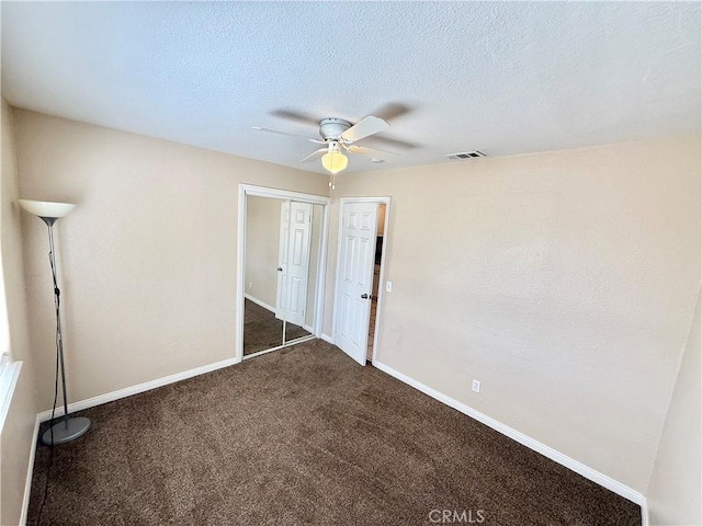 unfurnished bedroom featuring ceiling fan, dark carpet, a textured ceiling, and a closet