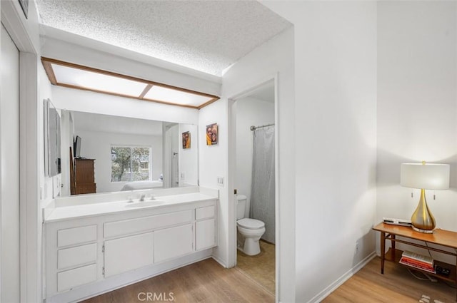 bathroom with a skylight, a textured ceiling, wood-type flooring, and toilet