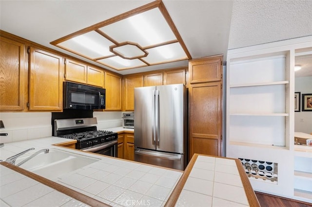 kitchen with stainless steel appliances, tile counters, kitchen peninsula, and sink