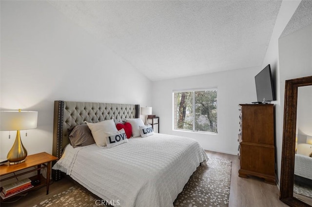 bedroom with vaulted ceiling, hardwood / wood-style floors, and a textured ceiling