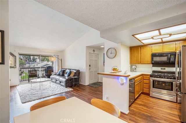 kitchen with lofted ceiling, a textured ceiling, appliances with stainless steel finishes, dark hardwood / wood-style flooring, and kitchen peninsula