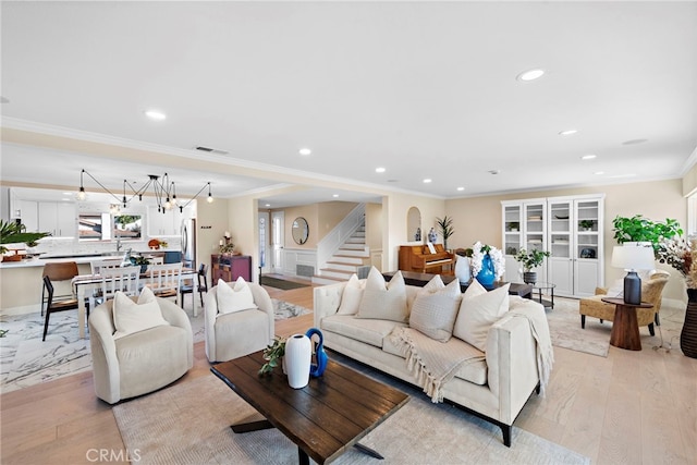 living room with crown molding, a chandelier, and light wood-type flooring