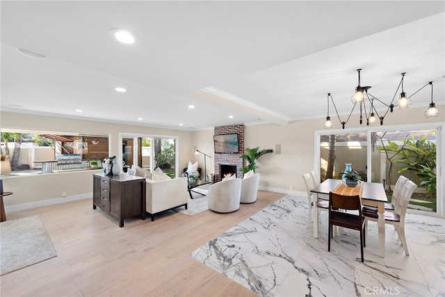 dining space featuring crown molding, a chandelier, light hardwood / wood-style floors, and a brick fireplace