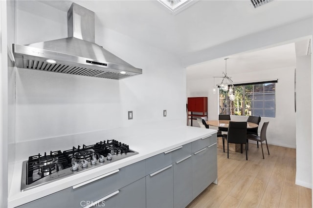 kitchen featuring pendant lighting, gray cabinetry, ventilation hood, stainless steel gas cooktop, and light wood-type flooring