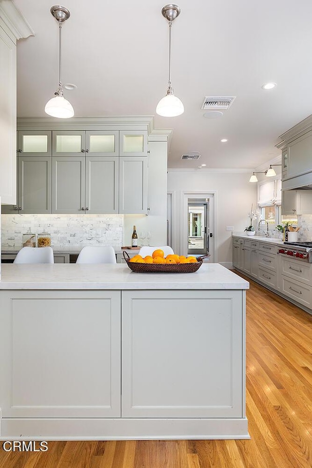 kitchen featuring sink, gray cabinetry, light hardwood / wood-style floors, hanging light fixtures, and tasteful backsplash