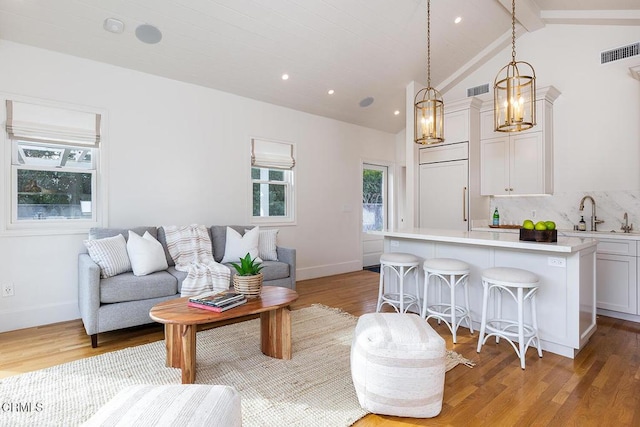 living room with sink, lofted ceiling with beams, and light hardwood / wood-style floors