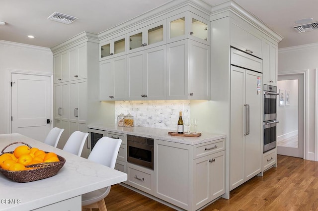 kitchen with crown molding, white cabinets, built in appliances, and light stone countertops