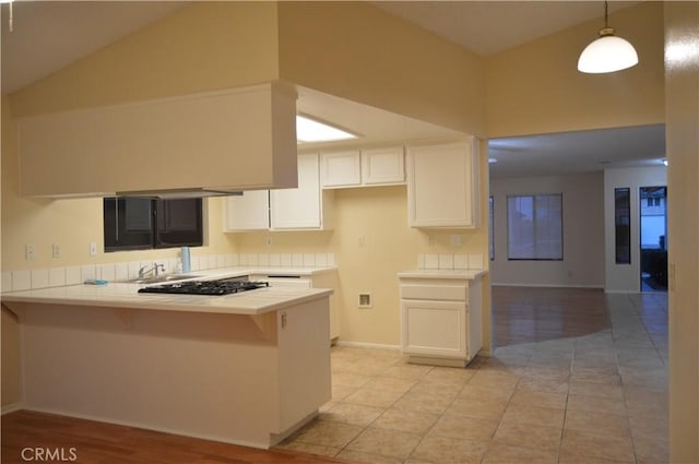 kitchen with lofted ceiling, white cabinetry, hanging light fixtures, kitchen peninsula, and stainless steel gas stovetop