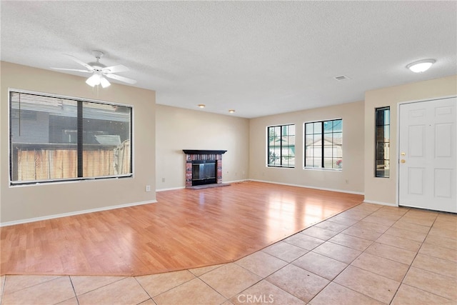 unfurnished living room featuring light tile patterned floors, visible vents, a ceiling fan, a brick fireplace, and a textured ceiling