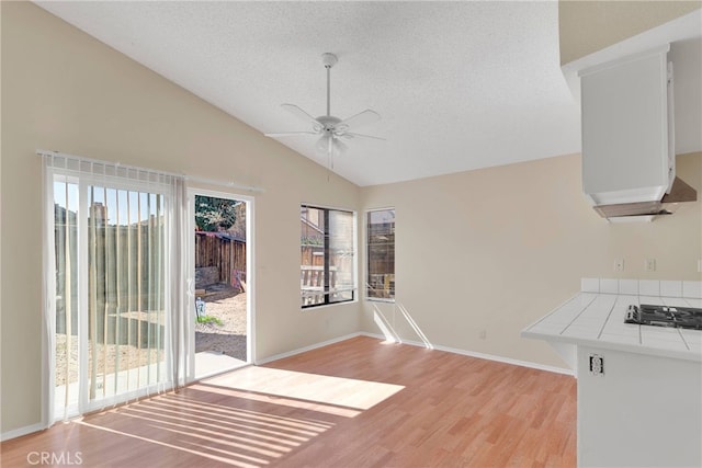 unfurnished dining area with ceiling fan, a textured ceiling, baseboards, vaulted ceiling, and light wood-style floors