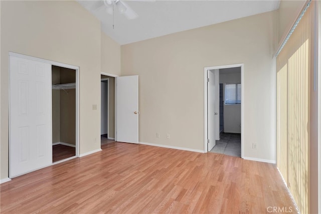 unfurnished bedroom featuring a closet, ensuite bathroom, light wood-style floors, high vaulted ceiling, and baseboards