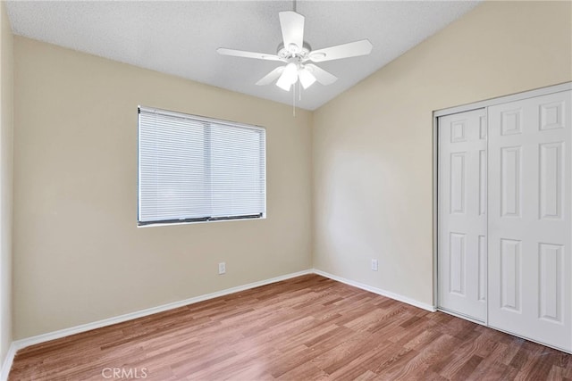 unfurnished bedroom featuring lofted ceiling, a ceiling fan, baseboards, light wood-style floors, and a closet