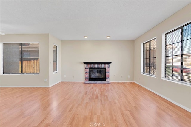 unfurnished living room with a textured ceiling, light wood finished floors, a fireplace, and baseboards