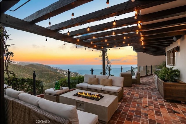 patio terrace at dusk featuring a pergola, a water and mountain view, and an outdoor living space with a fire pit