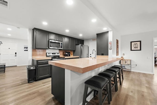 kitchen featuring backsplash, appliances with stainless steel finishes, a kitchen breakfast bar, and light hardwood / wood-style flooring