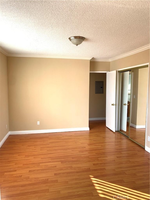 empty room with hardwood / wood-style flooring, ornamental molding, electric panel, and a textured ceiling
