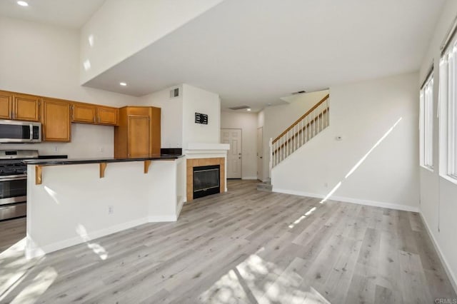 kitchen featuring appliances with stainless steel finishes, a breakfast bar, light hardwood / wood-style floors, and a tile fireplace