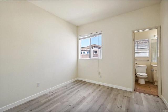 unfurnished bedroom featuring ensuite bath and light hardwood / wood-style floors