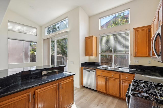 kitchen with sink, vaulted ceiling, light hardwood / wood-style flooring, dark stone countertops, and stainless steel appliances