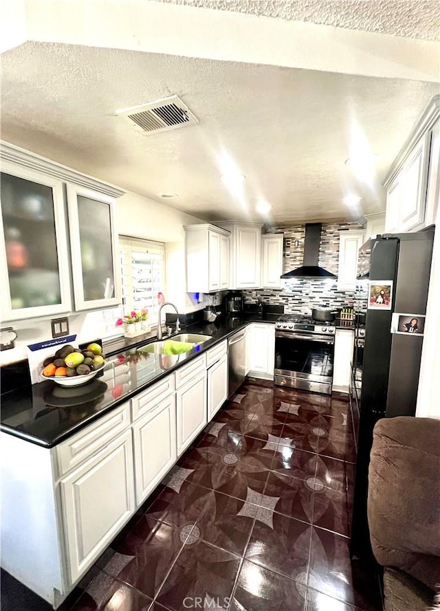 kitchen featuring wall chimney range hood, sink, appliances with stainless steel finishes, white cabinetry, and decorative backsplash