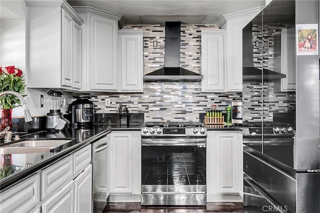 kitchen with white cabinetry, sink, stainless steel gas range oven, dark stone counters, and wall chimney range hood