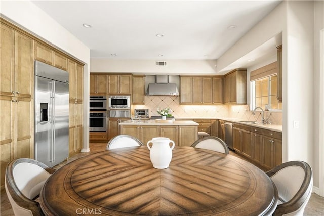 kitchen featuring sink, decorative backsplash, a center island, built in appliances, and wall chimney range hood