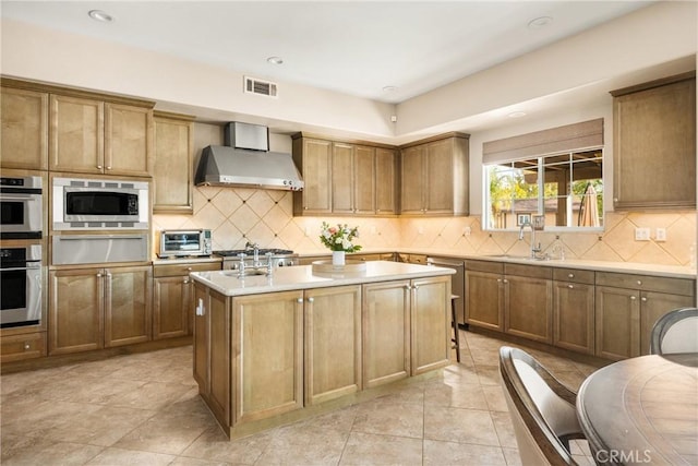 kitchen with appliances with stainless steel finishes, tasteful backsplash, an island with sink, sink, and wall chimney range hood