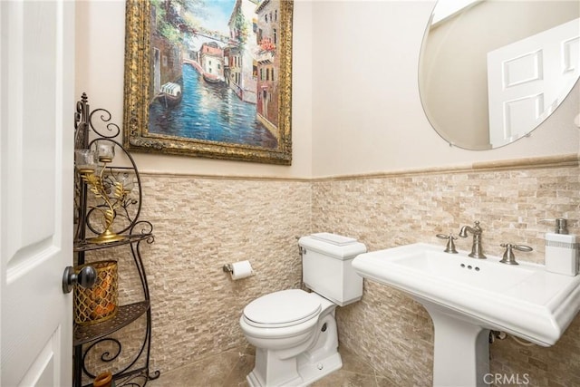 bathroom with toilet, tile patterned flooring, sink, and tile walls