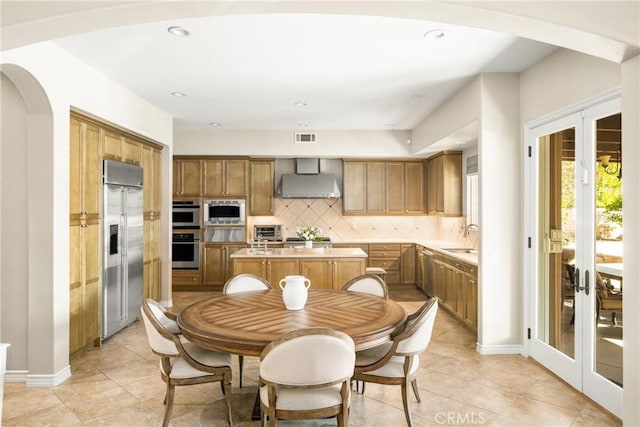 kitchen with tasteful backsplash, sink, built in appliances, wall chimney range hood, and french doors