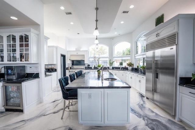 kitchen featuring pendant lighting, sink, a breakfast bar, stainless steel built in refrigerator, and an island with sink