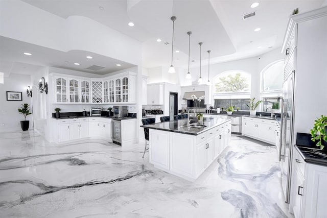 kitchen with hanging light fixtures, white cabinetry, a kitchen island with sink, and sink