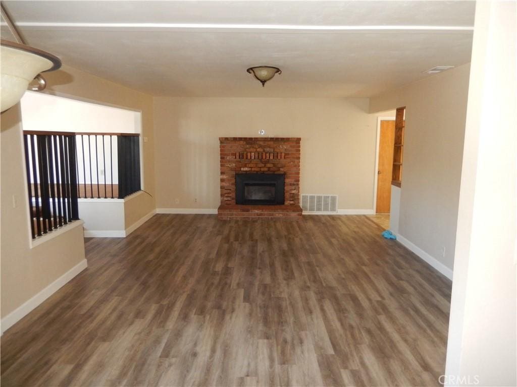 unfurnished living room with a brick fireplace and dark wood-type flooring