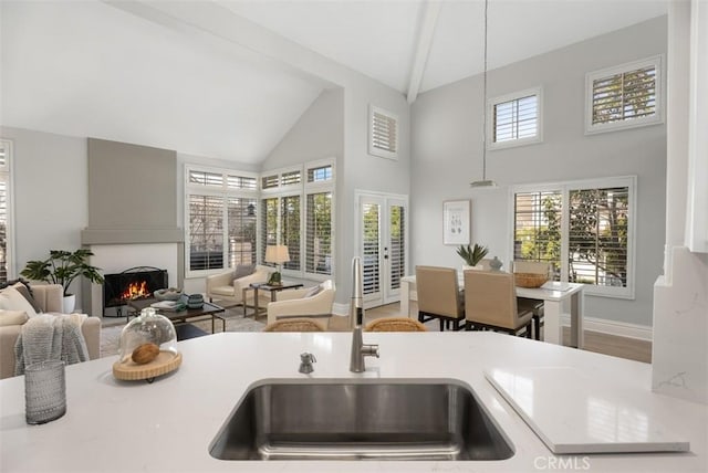 kitchen featuring sink, wood-type flooring, decorative light fixtures, high vaulted ceiling, and a large fireplace