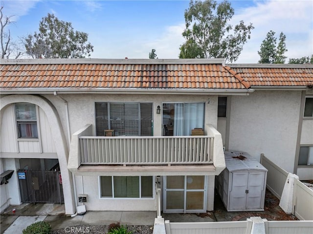 back of house featuring a tiled roof, fence, a balcony, and stucco siding