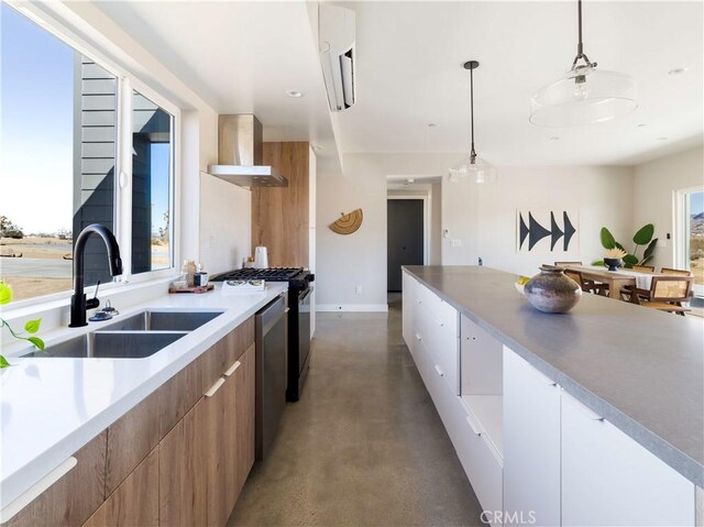 kitchen with concrete flooring, sink, white cabinetry, pendant lighting, and wall chimney range hood