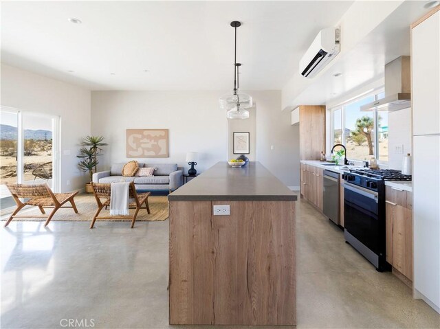 kitchen with appliances with stainless steel finishes, a kitchen island, a wall mounted AC, hanging light fixtures, and wall chimney range hood