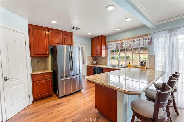 kitchen with visible vents, freestanding refrigerator, a sink, a peninsula, and a kitchen breakfast bar