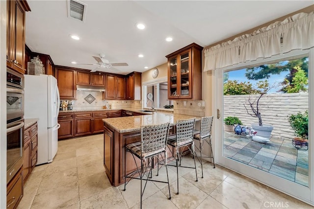 kitchen featuring sink, a kitchen bar, decorative backsplash, white refrigerator, and kitchen peninsula